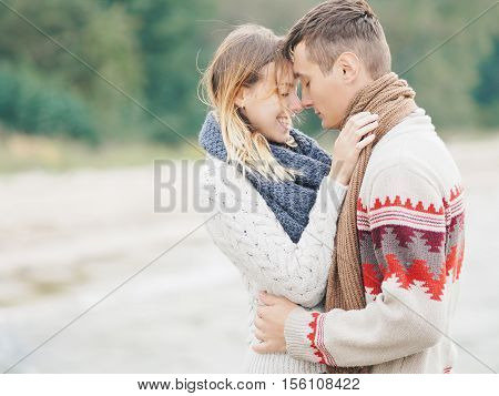 Young attractive couple in knitted sweaters on a cliff on sea shore hugging and holding hands creative toning