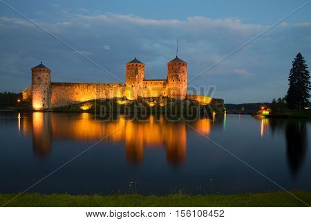 Old fortress of Olavinlinna on the Saimaa lake in night illumination in the August evening. Savonlinna, Finland