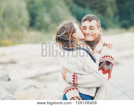 Young attractive couple in knitted sweaters on a cliff on sea shore hugging and kissing creative toning