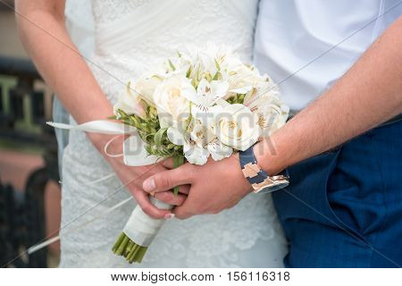 Hands newlyweds with a bouquet. A newly weding couple place their hands on a wedding bouquet