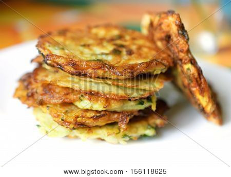 Stack of fried vegetable fritter made of zucchini eggs parsley decorated with a sprig of green onions on a white plate. Selective Focus Focus on the front of the top fritters