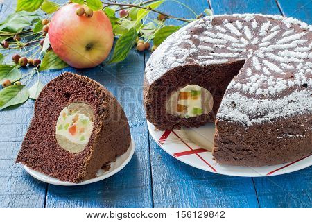 Baking in multicooker. Delicious homemade chocolate cake with whole apples curd and candied fruit on a blue wooden table. Selective focus