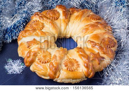 Creative homemade cake of yeast dough filled with cheese. The original festive cake in the form of a Christmas wreath on the background of branch Christmas tree with decoration on a blue background