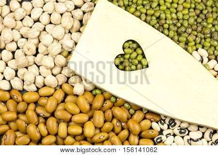 Wooden spoon with heart shape carved on colorful legumes