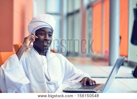 Sudanese business man in traditional outfit using mobile phone in office.