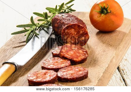 sliced hungarian kolbasz with rosemary and tomato on a wooden board