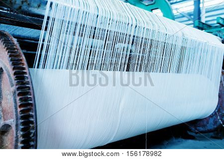 A row of textile looms weaving cotton yarn in a textile mill.