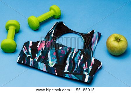 Sports equipment including colorful sportswear green dumbbells and apple isolated on blue background. Copy space.