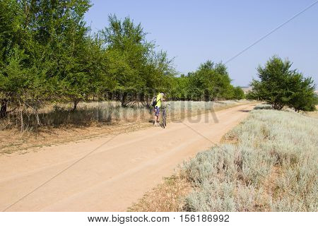 Man on the old bike is traveling across the steppe. The road in the desert in the summer. Volgograd region Russia