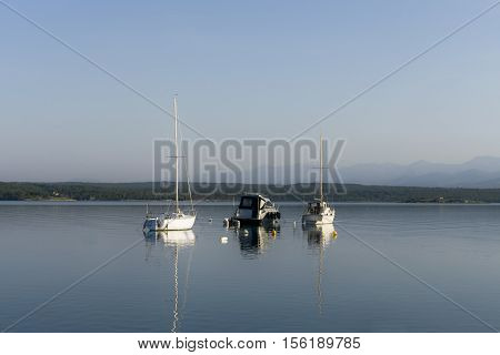 Three small boats / yachts achored in a safe bay in the morning calm sea