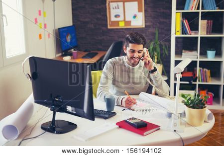 Young man working on computer talking on landline phone