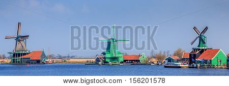 3 Dutch windmills next to the river against a clear blue sky