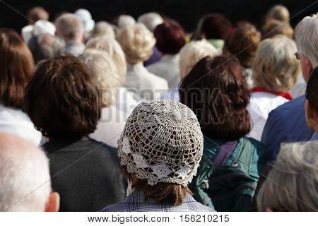 A crowd of people watching something. Composition of rhythmic adult heads. Short dark and gray hair. One head with a hat.