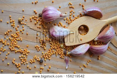 Cloves of garlic mustard seeds and spoon on wooden board. Rustic style garlic on vintage wooden background. Fresh garlic clove. Garlic bulbs.