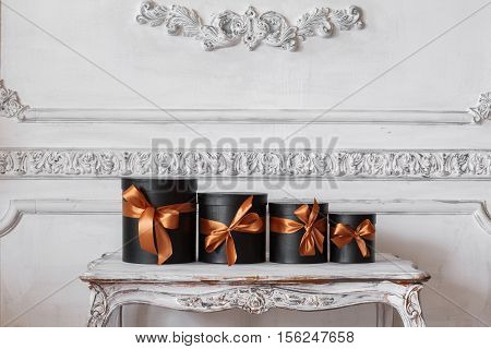 Wrapped gift black boxes with ribbons as Christmas presents on a table on luxury white wall design bas-relief stucco mouldings roccoco elements.