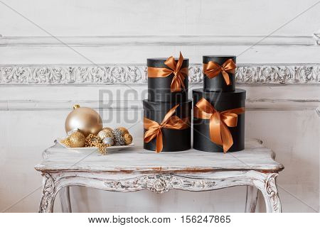 Wrapped gift black boxes with ribbons as Christmas presents on a table on luxury white wall design bas-relief stucco mouldings roccoco elements.