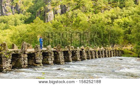 Tourist woman standing on stone slab bridge Terland Klopp in Norway Dalane region.
