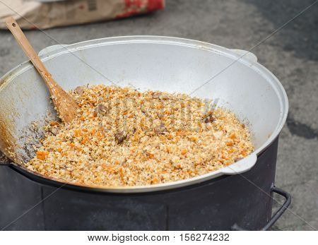 Pilaf in cauldron. A delicious pilaf with pork, carrots and rice with spicy spices and onions, in a cauldron with a wooden spatula. Close-up.