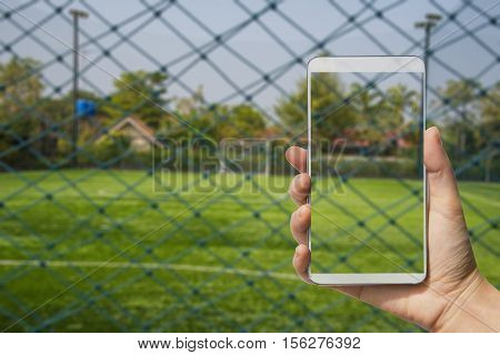 Double exposure hand holding a modern phone with soccer or football on screen,Blur image of football field with copy space