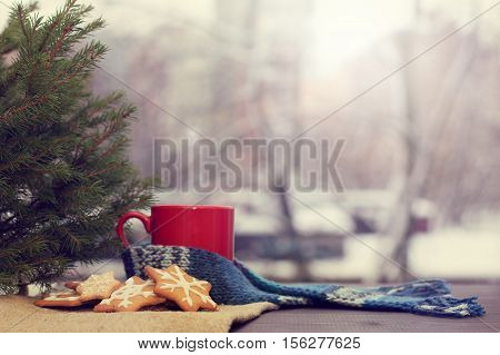 cookies in the form of snowflakes on a table near a Christmas tree and red mug on a background of a winter landscape outside the window / awaiting a holiday