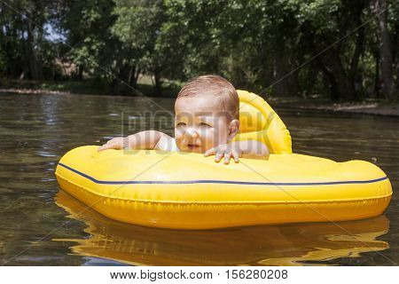 Baby boy with yellow rubber ring on natural river pool