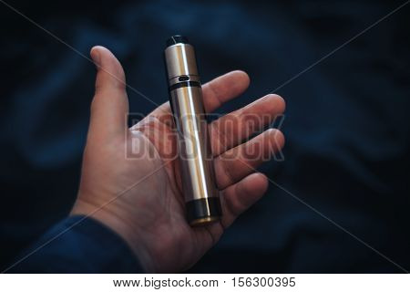 Vaping device in in the man's hand. Electronic cigarette, vape. Mech mod, sub-ohm.