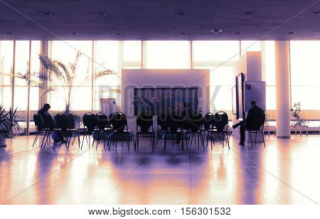 Special toned photo with silhouettes of few people sitting on chairs in modern auditorium waiting for seminar to begin