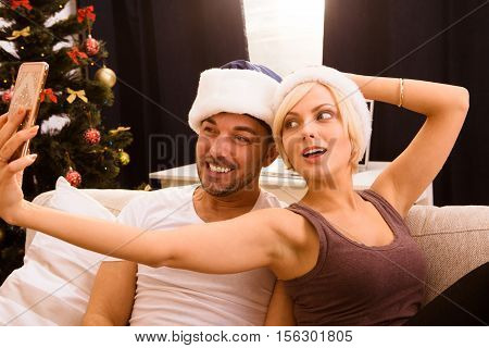 Picture of happy Christmas couple making self photos on mobile or smart home while celebraring New Year or Christmas at home