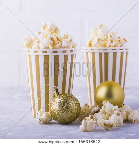 Salty fresh crusty homemade popcorn in silver paper cup in the fashion light background of white brick wall in a New Year's interior with silver Christmas balls. selective focus