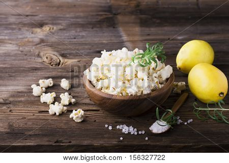 Salty crunchy fresh homemade popcorn flavored with lemon peel and rosemary scent in a wooden bowl on a simple wooden background. The concept of natural homemade organic seasonal food. selective focus