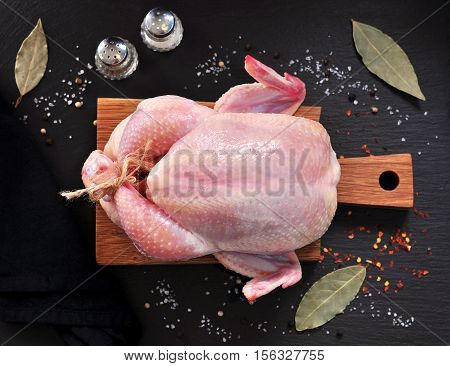Raw chicken with spices on a wooden board on a black stone.