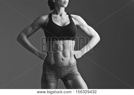 Closeup of fit woman torso with abs muscles. Body part. Fitness. Sudio shot over grey background. Monochrome.