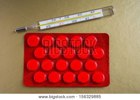 Medical thermometer and pills in red packaging. The medicine and diagnosis of diseases.