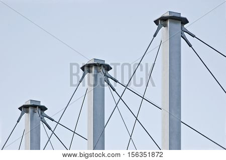 Tied Suspension Roof Cables, Three Tall Grey Masts, Cable-suspended Swooping Rooftop Pylon Anchors, Pale Blue Summer Sky, Large Detailed Horizontal Closeup, Contemporary Construction Concept