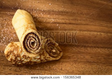 Crepe rolls filled with cinnamon and sugar photographed overhead on wood with natural light (Selective Focus Focus on the front of the upper roll)