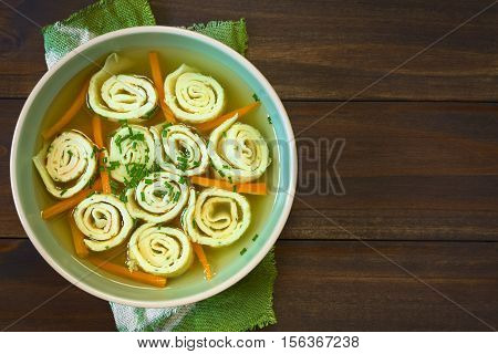 Traditional German Flaedlesuppe and Austrian Frittatensuppe based on consomme with rolls or stripes of pancake or crepe garnished with chives photographed overhead on wood with natural light (Selective Focus Focus on the soup)