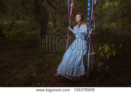 Fabulous retro woman in a smart dress in the woods sitting on a swing.