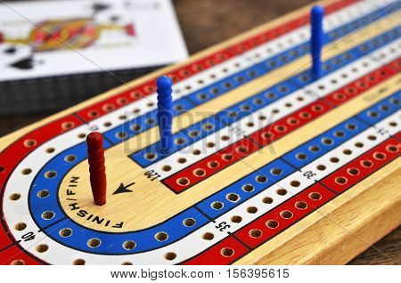 A low angle image of a wooden cribbage board with the red cribbage peg in the winning position and the jack of spades in the background.