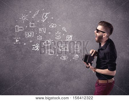 An elegant hipster guy trying to use a vintage camera with camera settings icons drawn on wall, like flash, white balace or ISO value concept