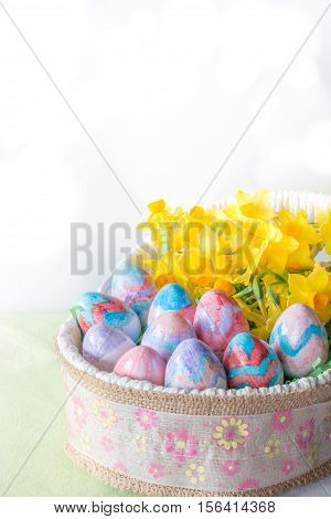 Basket of Hand Painted Easter Eggs with Daffodils on Table Vertical with Copy Space & Bokeh