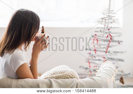 Young beautiful woman drinking hot chocolate with marshmallow in christmas decorated home. Holiday concept