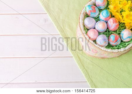 Basket of Hand Painted Easter Eggs with Daffodils on Table From Above with Copy Space