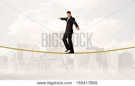 A young elegant businessman walking on tight golden rope in front of city buildings landscape background concept