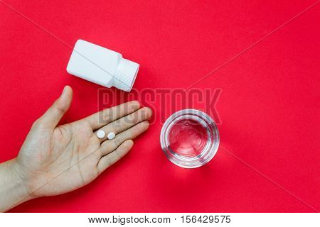 Top view pills on hand with pill bottle and water on red background.Take a medicine concept.