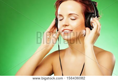 Young happy woman listening to music with headhones over green background