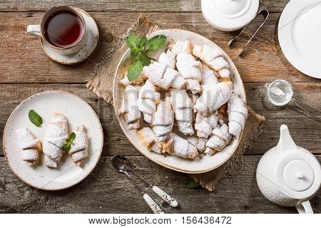 Rugelach with jam filling on plate with tea on wooden background, top view with copy space