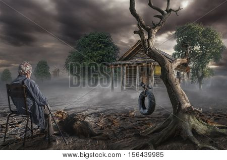 an elderly gray-haired man sits near a dry tree on the spot where was the house of his childhood