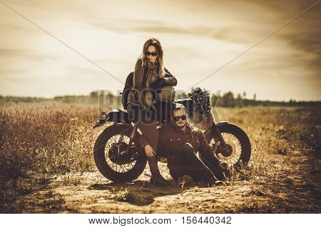 Stylish cafe racer couple on the vintage custom motorcycles in a field.