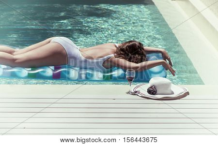 female in a swimsuit lying near the pool with hat and wine