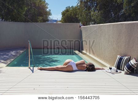 female in a swimsuit lying near the pool with hat and wine
